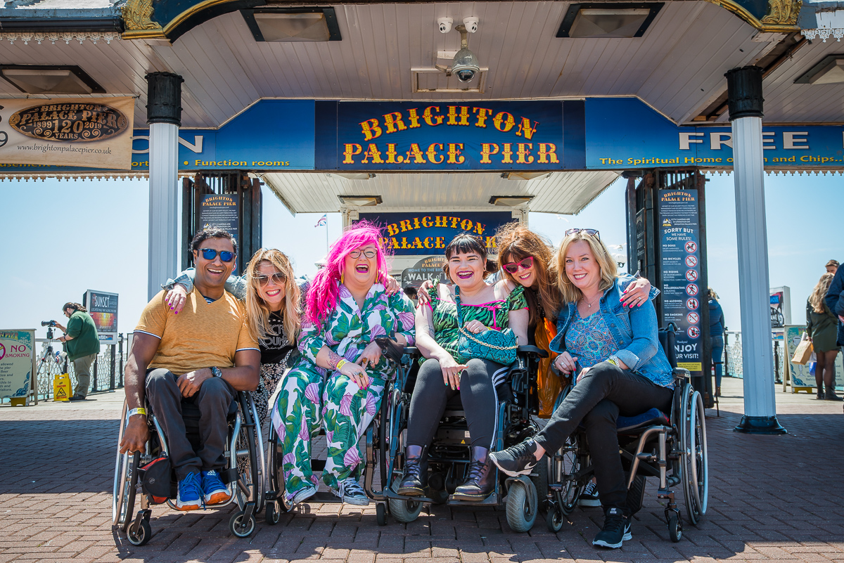 Group of 6 Enhance the UK trainers most of whom are wheelchair users posing together in front of Brighton Pier Sign