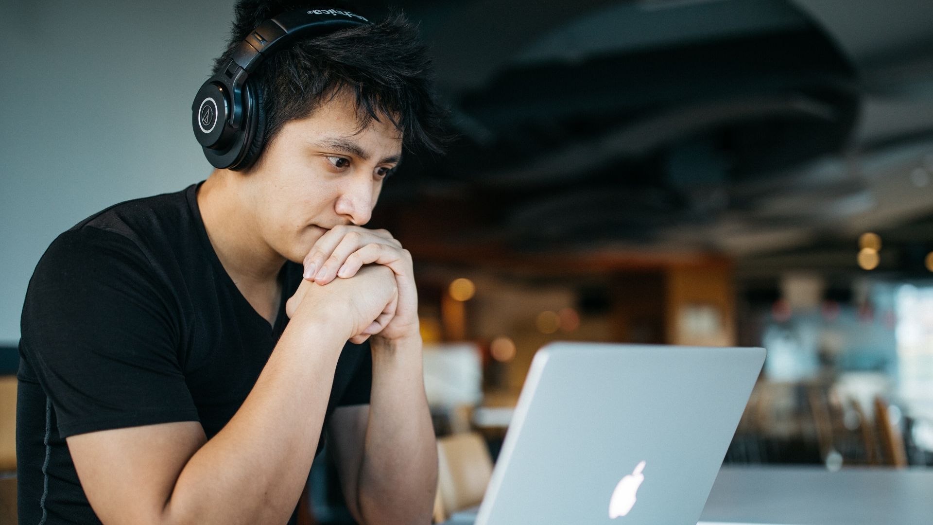 accessible video calls - a man sits in front of his laptop screen wearing headphones and a black tshirt, his hands are together with his chin resting on them