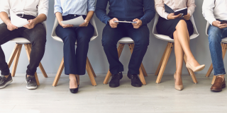 5 people sitting on chairs in a row. Some are wearing trousers and one a skirt.