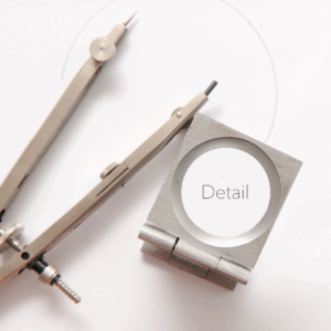 Magnifying glass with 'detail' inside and two graphic design pencils