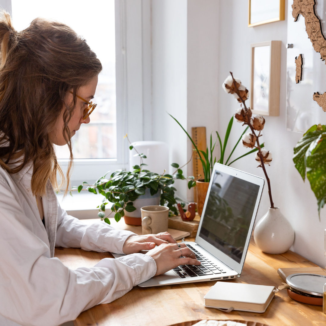 woman sitting on her laptop at a desk with flowers and plants on it